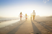 Happy family walking into distance, holding hands, on sunny beach创意图片素材 - Juice Images