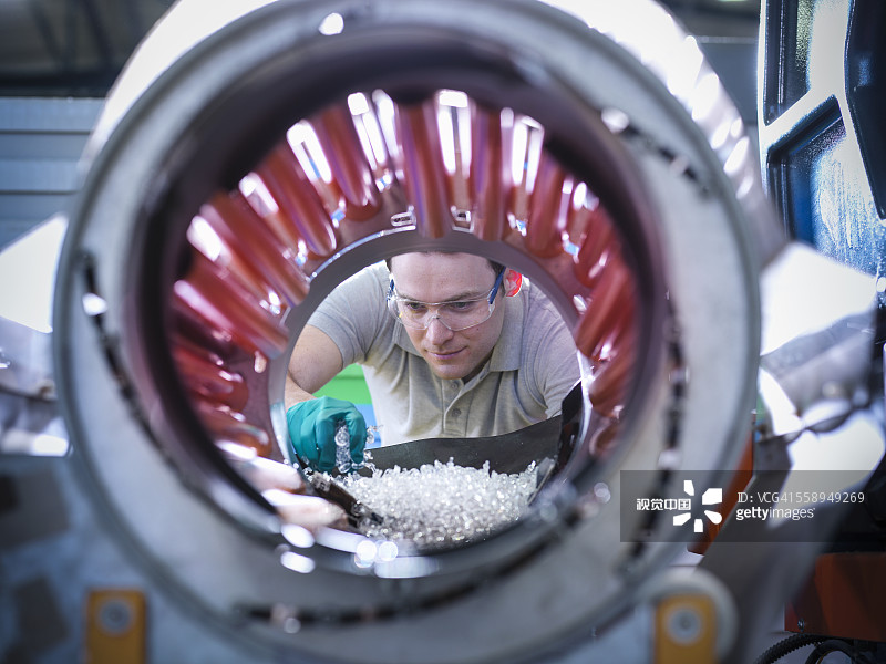 Worker inspecting parts from plastic injection moulding machine in plastics factory
