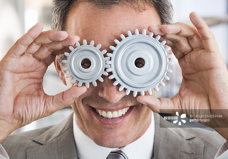 Business man holding cogs to his eyes