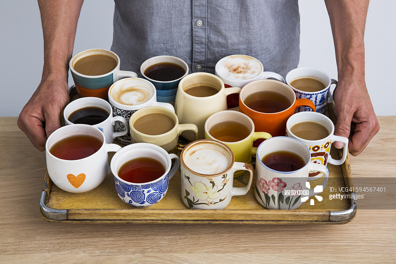 Man holding a tray of many cups of coffee and tea