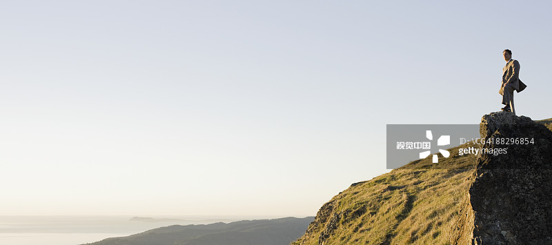 Businessman standing on rock overlooking ocean
