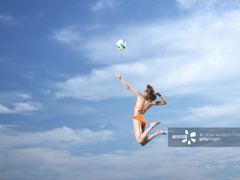 Young woman hitting volley ball jumping in sky