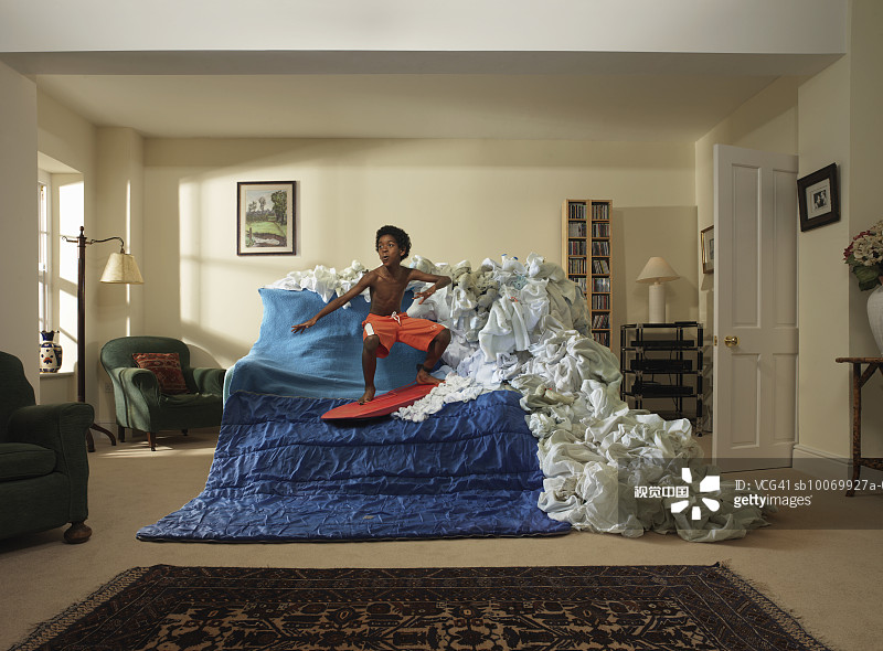 Boy (8-9) pretending to surf wave created from sheets on sofa