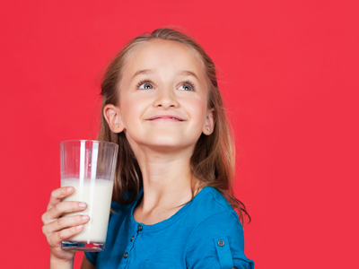 Young girl holding glass of milk while looking up on red background gettyimages图片素材